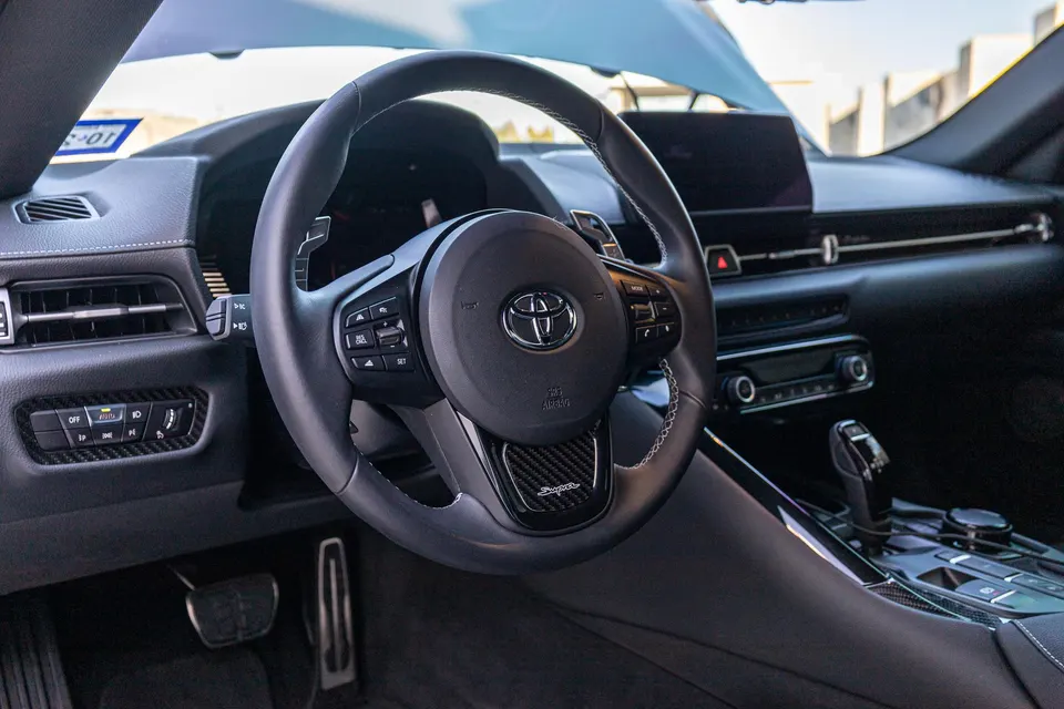 Detailed view of the Toyota Supra's interior, featuring the steering wheel with paddle shifters and carbon fiber trim.