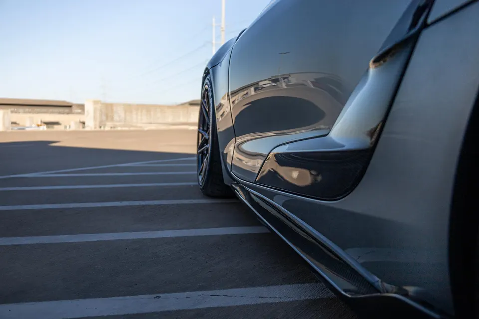 Close-up of a performance car's side profile, showcasing the wheel, fender, and carbon fiber side skirt in a parking lot.