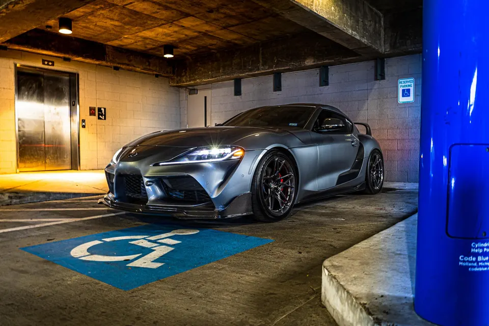 Grey Toyota Supra with aftermarket wheels and a front splitter parked in an underground garage.