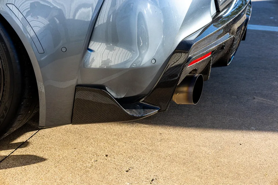 Close-up of a grey car's rear bumper featuring a carbon fiber diffuser and a large, single exhaust tip.