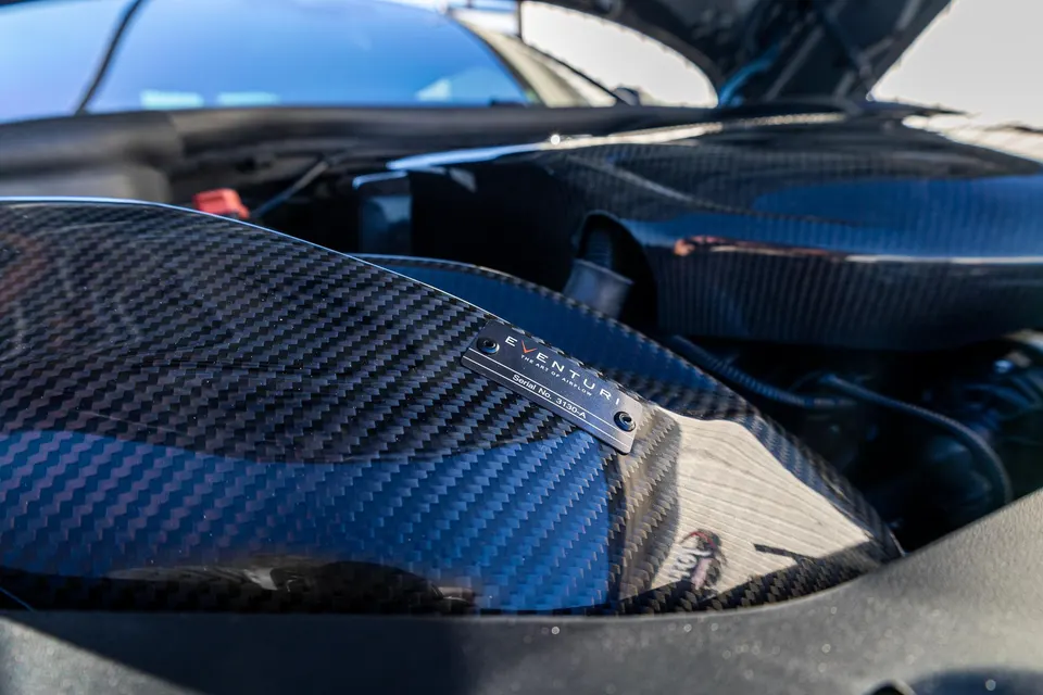 Close-up of an Eventuri carbon fiber intake system with a serial number plate in a car's engine bay.