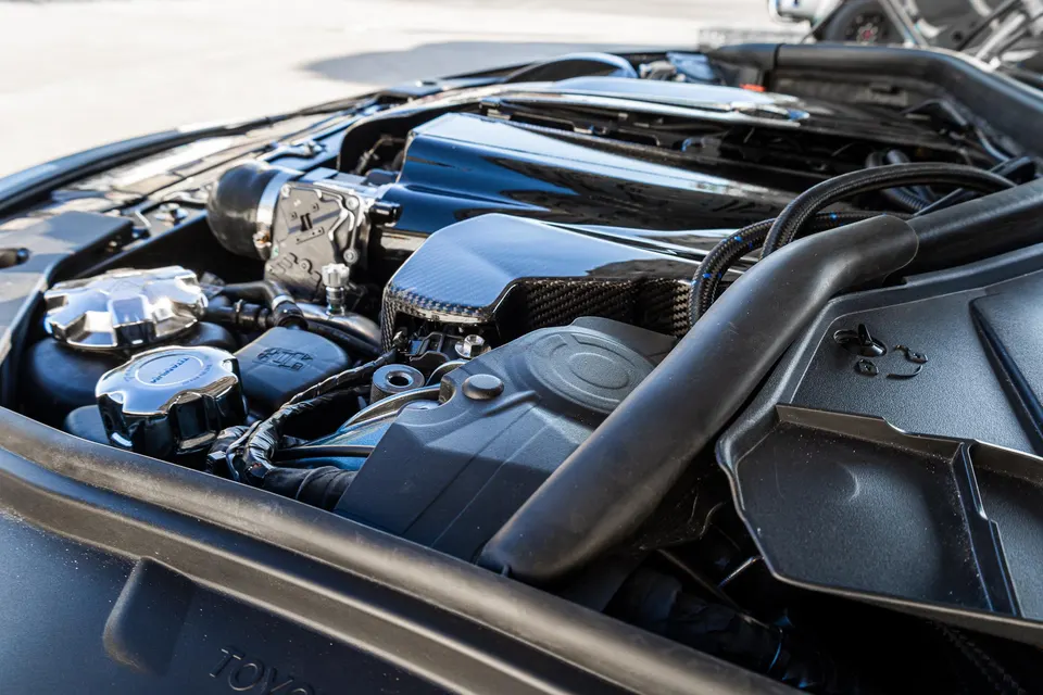 A close-up view of a high-performance engine bay featuring a carbon fiber intake system and polished caps.