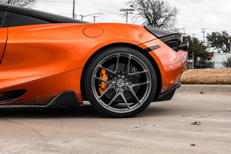Close-up of an orange McLaren's rear wheel, featuring HRE wheels and orange carbon ceramic brakes.