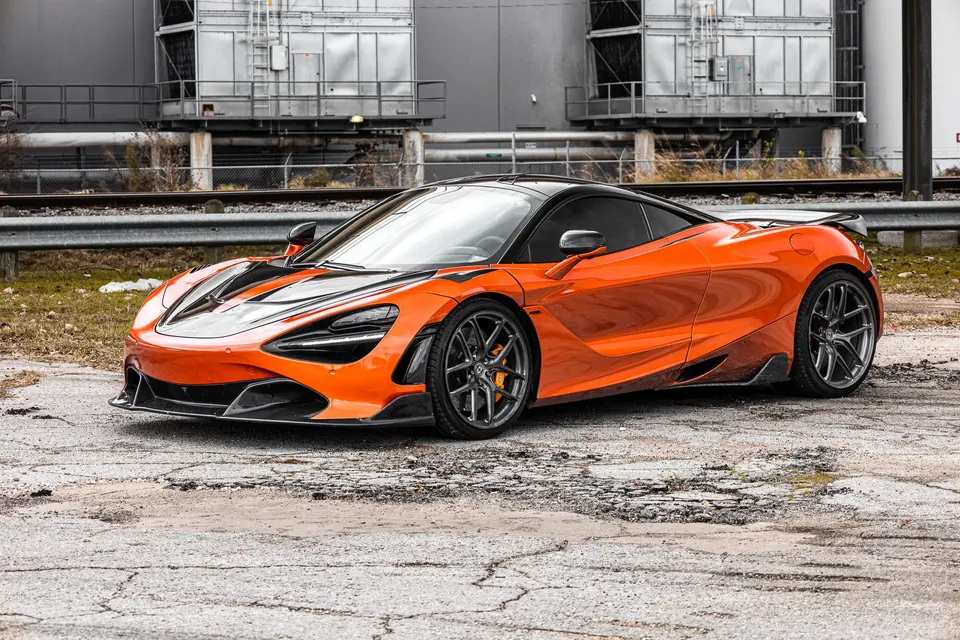 Orange McLaren 720S with black accents and aftermarket wheels parked in an industrial setting.