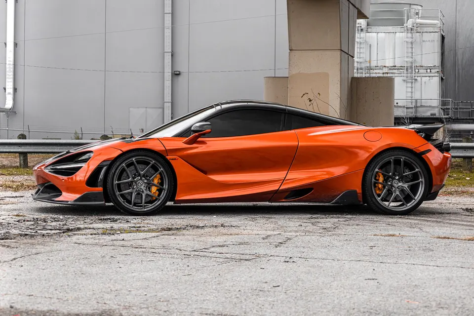 Orange McLaren 720S with HRE wheels and carbon fiber aero parked in an industrial setting.