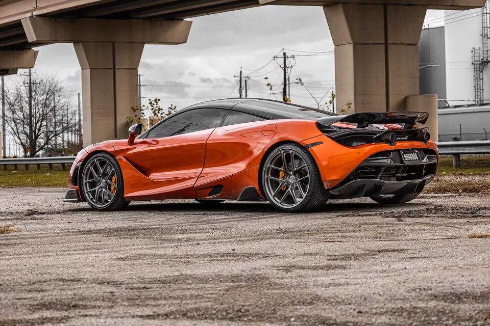 Orange McLaren 720S with aftermarket wheels and carbon fiber aero parked under an overpass.