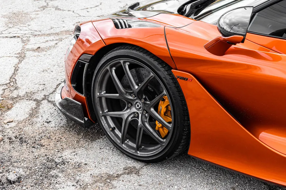 Close-up of an orange McLaren 720S front wheel with HRE performance wheels and yellow brake calipers.