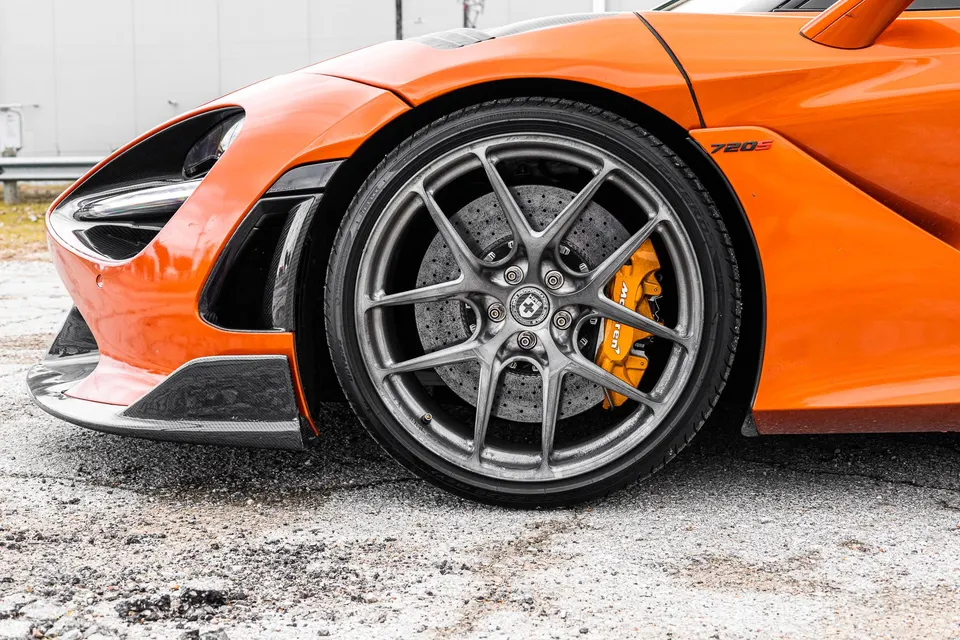 Close-up of an orange McLaren 720S front wheel, featuring custom HRE wheels and orange brake calipers.