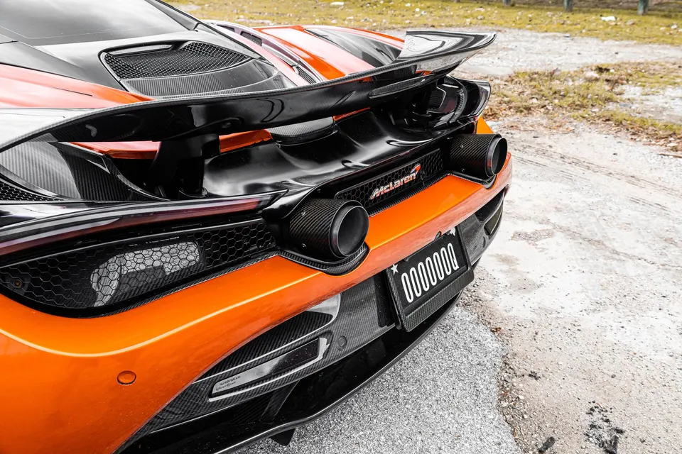 Rear view of an orange McLaren supercar showcasing its carbon fiber rear wing, exhaust tips, and diffuser.
