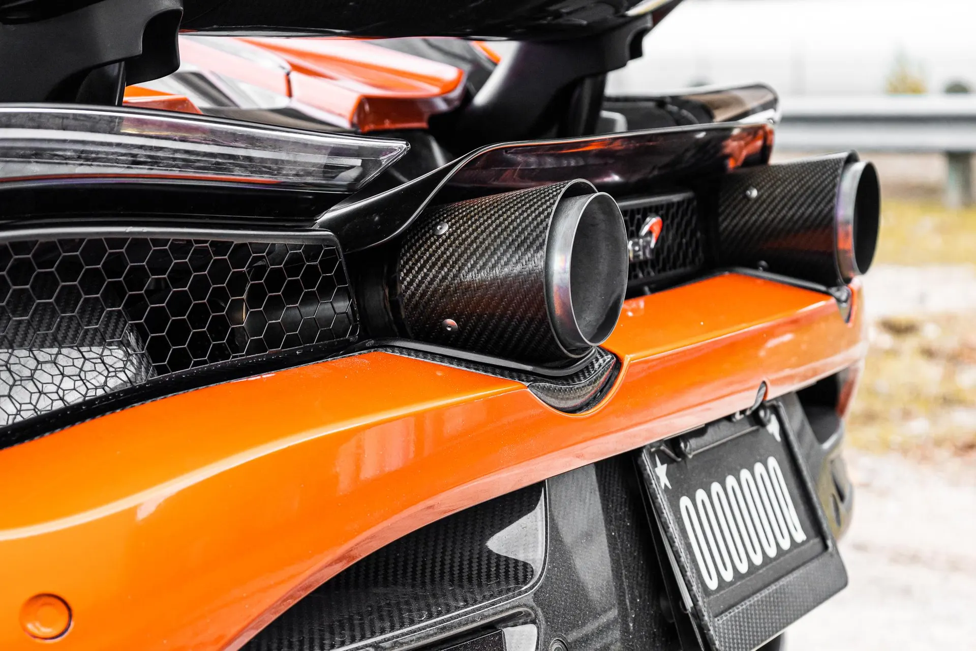 Close-up of the rear of an orange McLaren supercar, showcasing carbon fiber exhaust tips and diffuser.