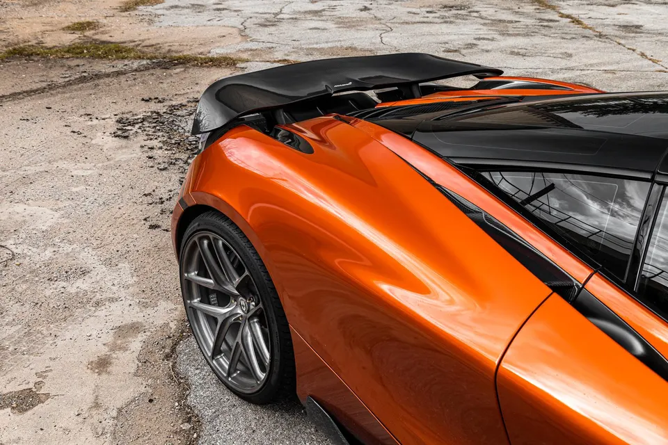Rear quarter view of an orange McLaren with a carbon fiber rear wing and custom multi-spoke wheels.