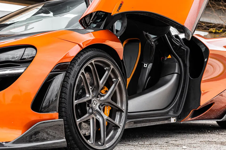 Close-up of an orange McLaren 720S showcasing its custom wheels, carbon fiber aero, and orange brake calipers.