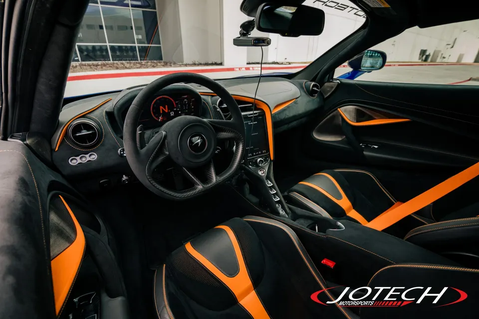 Interior view of a McLaren with black and orange seats, dashboard, and steering wheel, featuring a radar detector.