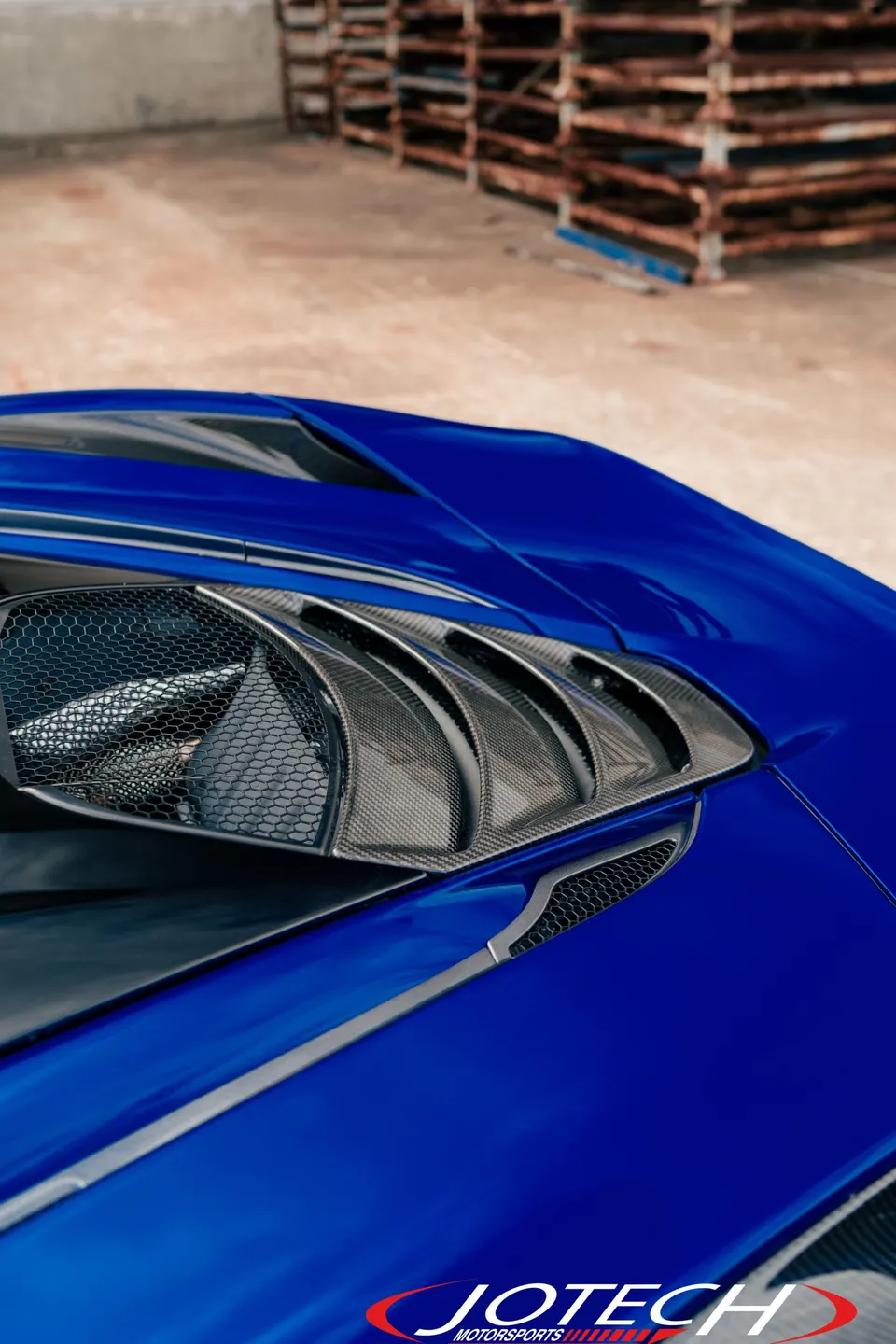 A close-up detail shot of a blue supercar's carbon fiber exterior vents.