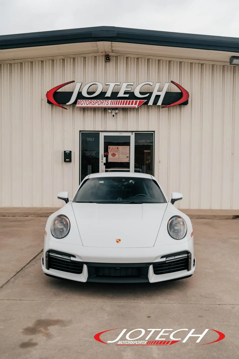 White Porsche 911 parked directly in front of the Jotech Motorsports performance tuning shop entrance.