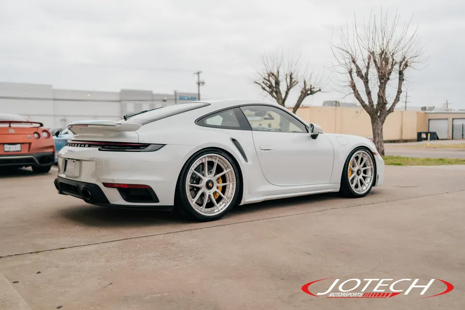White Porsche 911 with aftermarket multi-spoke wheels and yellow brake calipers parked outdoors.