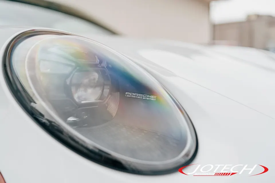 A close-up detail of a white Porsche's LED Matrix System headlight, showing reflections.