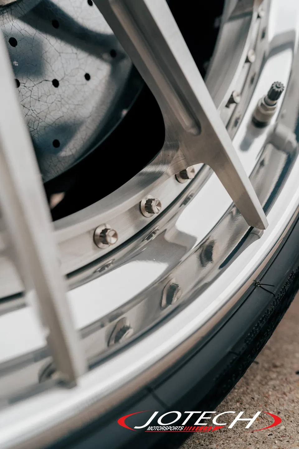 A close-up detail shot of a custom multi-piece wheel with a polished lip, showing the tire and a drilled brake rotor.