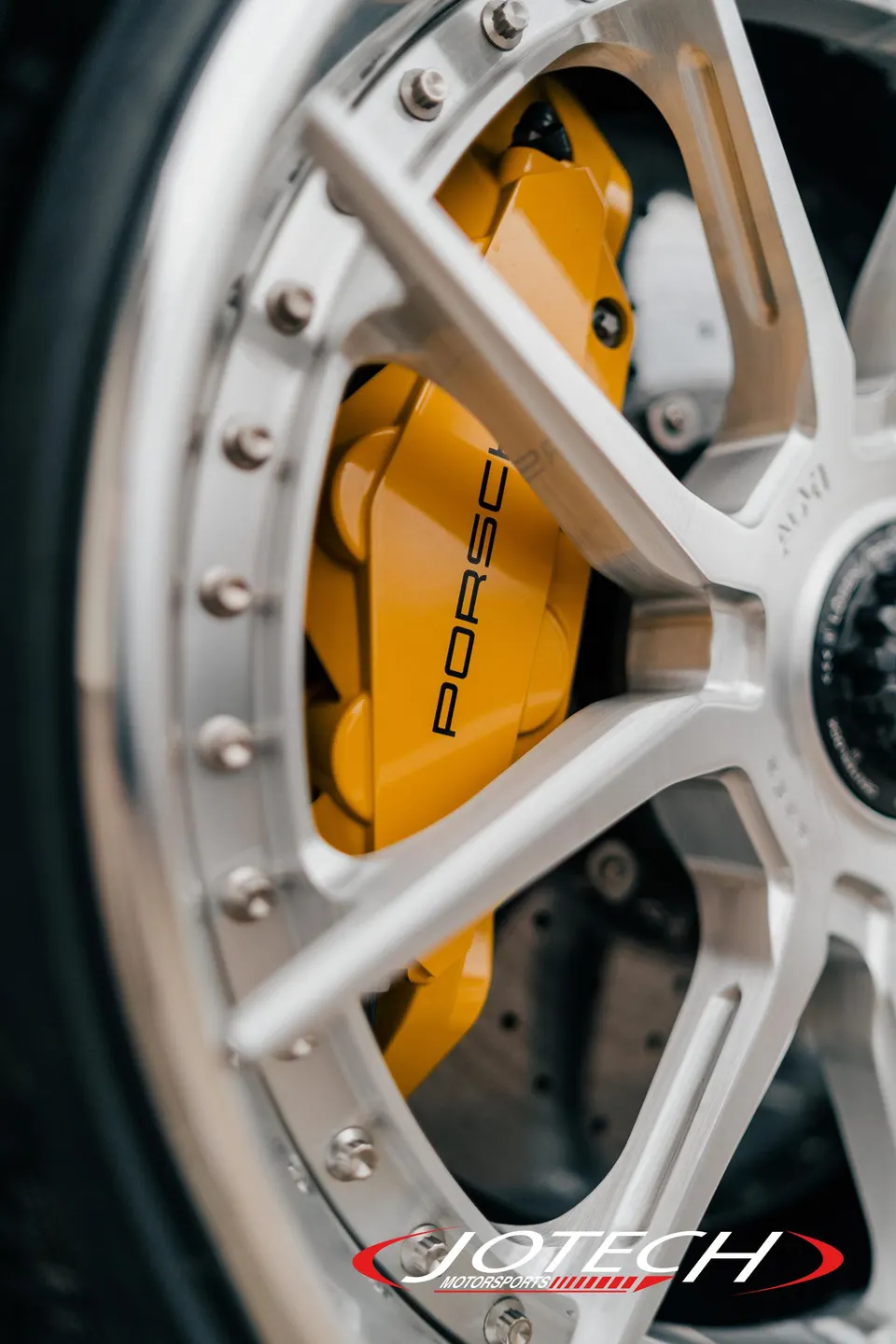 Close-up of a Porsche's yellow brake caliper with black lettering and a silver multi-spoke wheel.