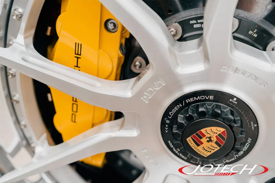Close-up of a silver ADV.1 wheel with a yellow Porsche brake caliper and centerlock hub.