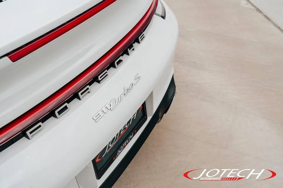 Close-up detail of the rear of a white Porsche 911 Turbo S, showing the PORSCHE and 911 Turbo S badging.