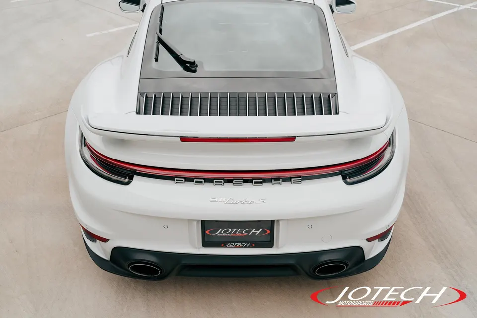 A white Porsche 911 Turbo S from the rear, showcasing its sleek design, rear spoiler, and dual exhaust tips.