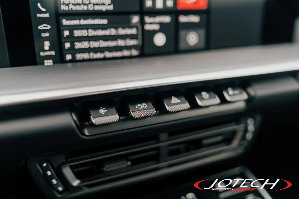 Close-up of a Porsche interior dashboard showing control buttons and an infotainment screen with navigation details.