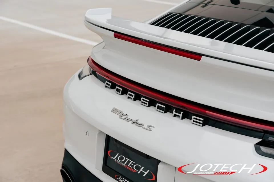 Close-up of the rear of a white Porsche 911 Turbo S, showing the badging, taillight, and rear spoiler.