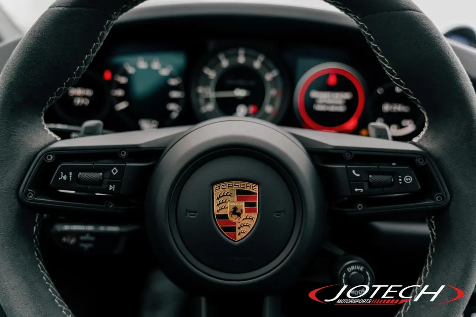 Close-up of a Porsche interior, showing the alcantara steering wheel with the Porsche crest and dashboard.