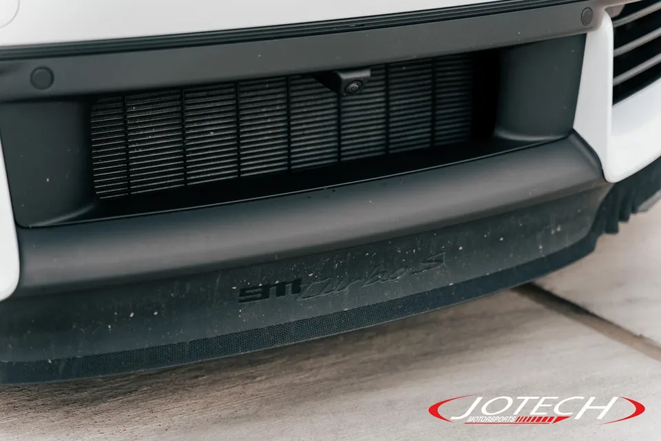 Close-up of the front bumper and lower grille of a white Porsche 911 Turbo S, showing the front camera and parking sensor.