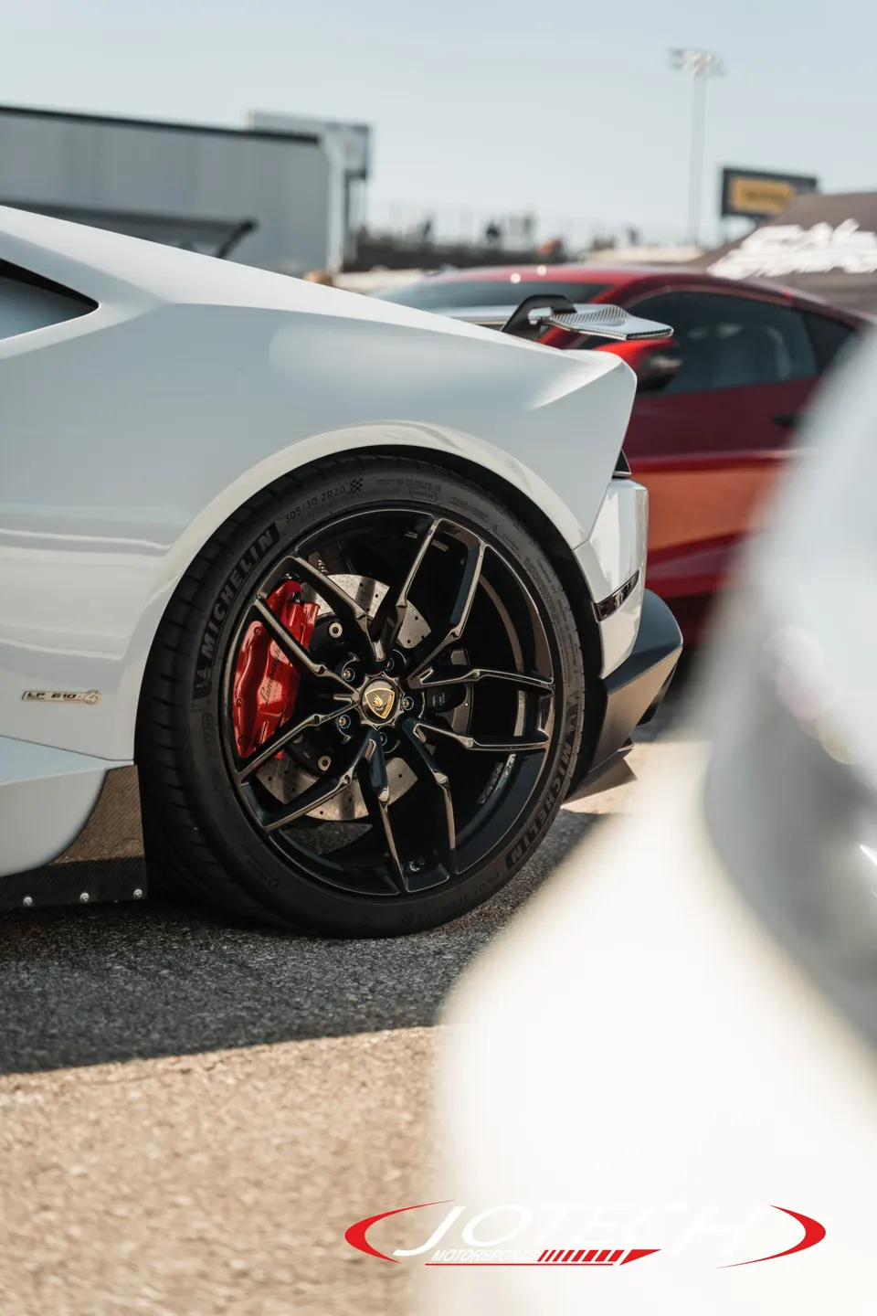 A white Lamborghini Huracan with black multi-spoke wheels and red brake calipers parked at a track.