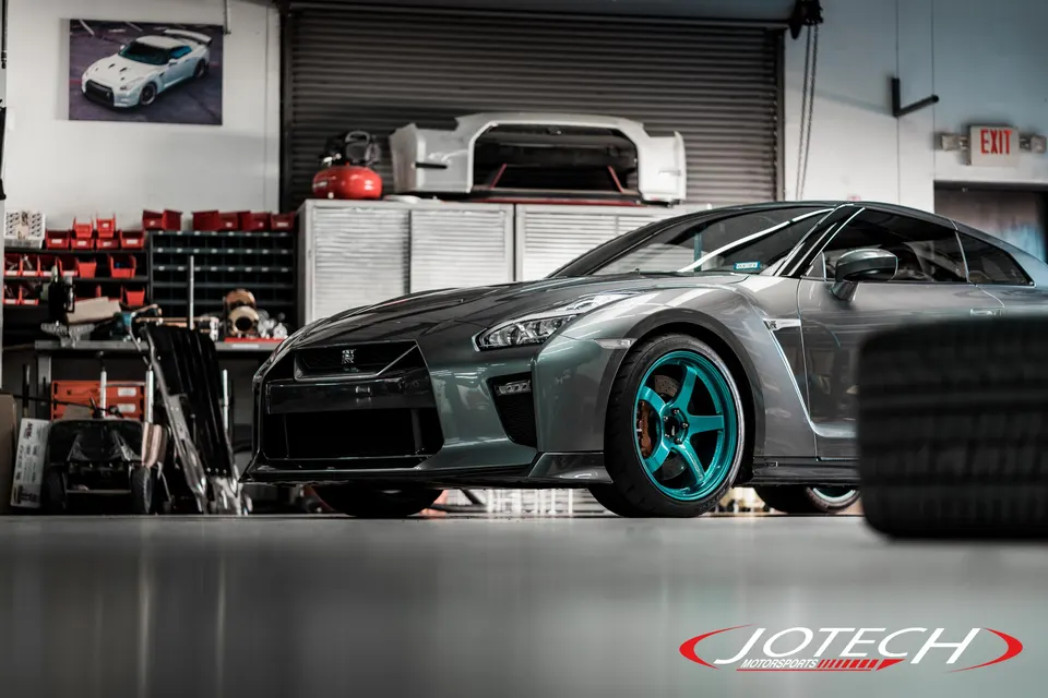 A grey Nissan GT-R with teal custom wheels parked in a performance tuning shop.