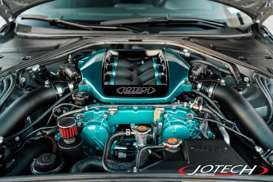A detailed view of a Jotech Motorsports built VR38DETT engine bay with a custom teal intake manifold and red air filter.
