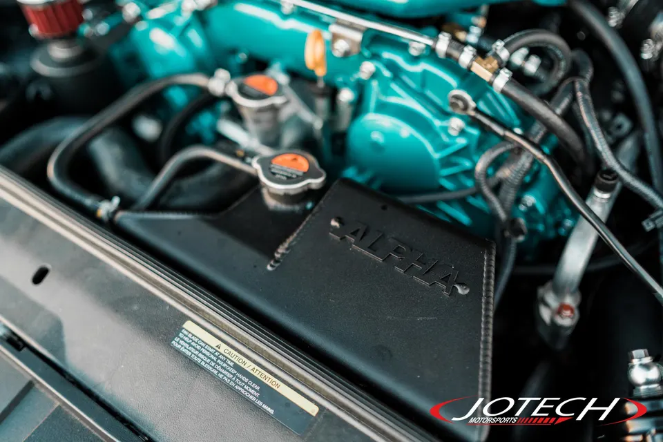Close-up of a custom engine bay with a teal engine block and an Alpha Performance intake system.