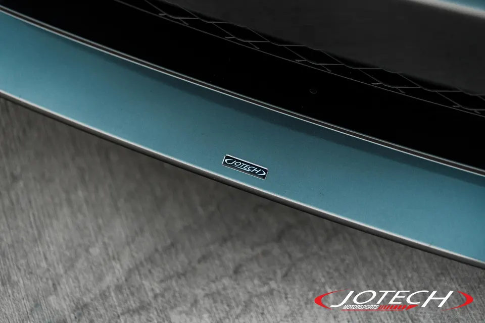 Close-up of a Jotech badge on a teal front splitter of a performance car, showcasing exterior detail.