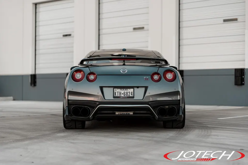 Rear view of a grey Nissan GT-R R35 showcasing its custom exhaust tips and rear diffuser in front of garage doors.