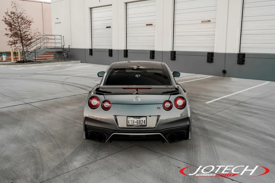 A grey Nissan GT-R R35 parked in a commercial lot, showcasing its rear design and quad exhaust.