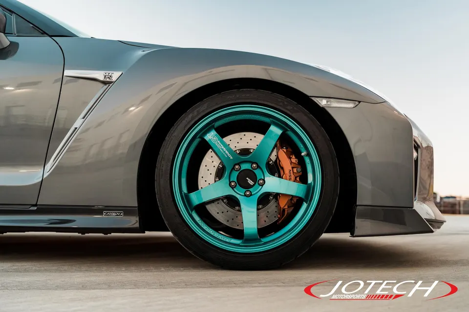 Close-up of a grey Nissan GT-R featuring teal Advan GT wheels and orange Nissan brake calipers.