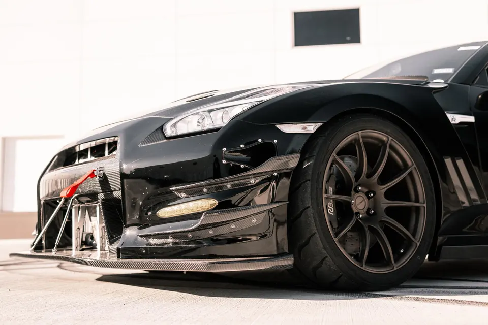 Close-up of a black Nissan GT-R with a carbon fiber front splitter, canards, and aftermarket wheels.