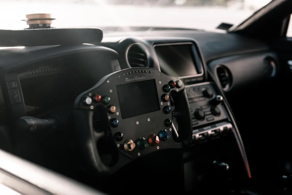 Close-up of a custom RaceGrade racing steering wheel with a digital display and multiple buttons inside a performance car.