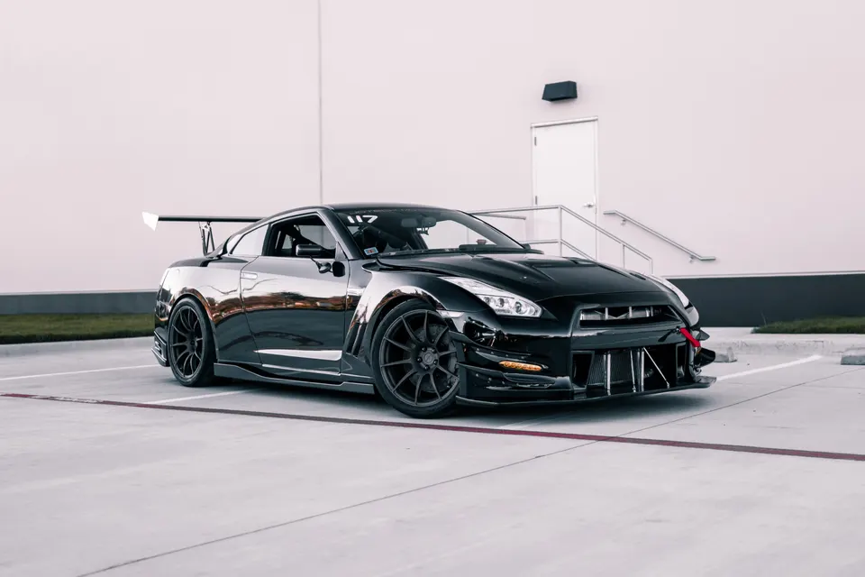 Black widebody Nissan GT-R with a large rear wing and aftermarket wheels parked in a lot.