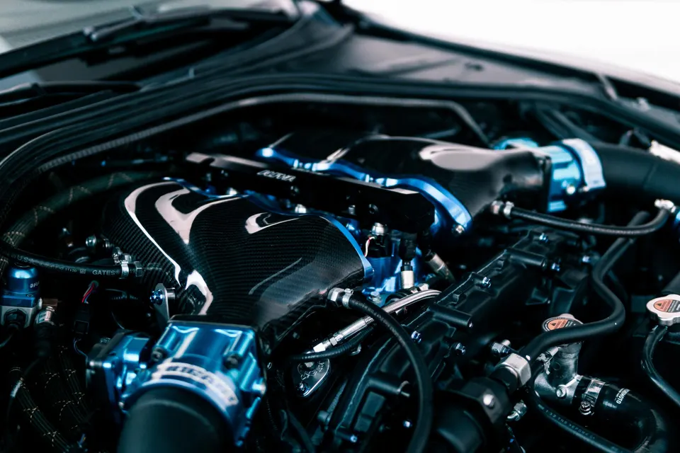 Close-up of a custom engine bay featuring a carbon fiber intake manifold and blue aftermarket fuel rails.