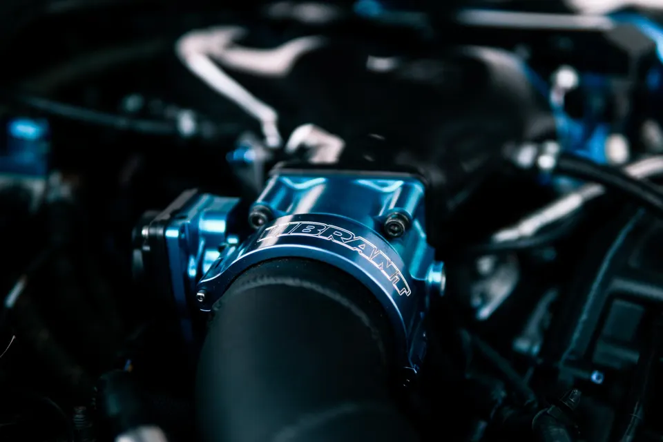 Close-up of a blue Vibrant Performance throttle body or intake component in a car's engine bay.