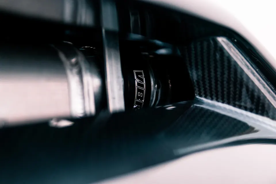 Close-up of a VIBE branded suspension component next to a carbon fiber panel on a performance car.