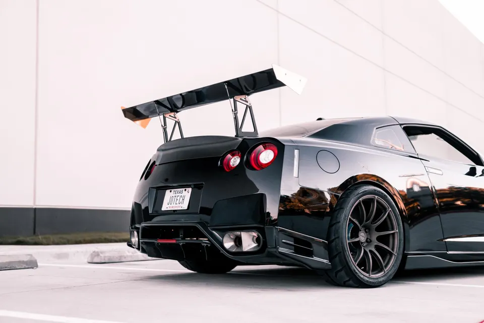 A black Nissan GT-R with a large carbon fiber wing and aftermarket wheels parked outdoors.