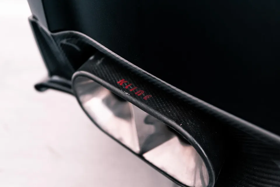 Close-up of a carbon fiber exhaust tip and diffuser with red lettering on a performance car.