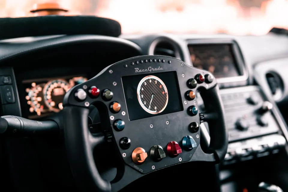 Close-up of a RaceGrade performance steering wheel with an integrated digital dash in a Nissan GT-R interior.