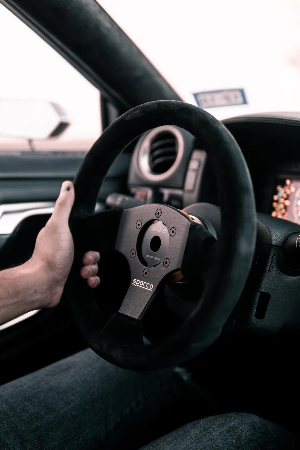Driver's hand on a Sparco QR-03 Series custom steering wheel in a performance car interior.