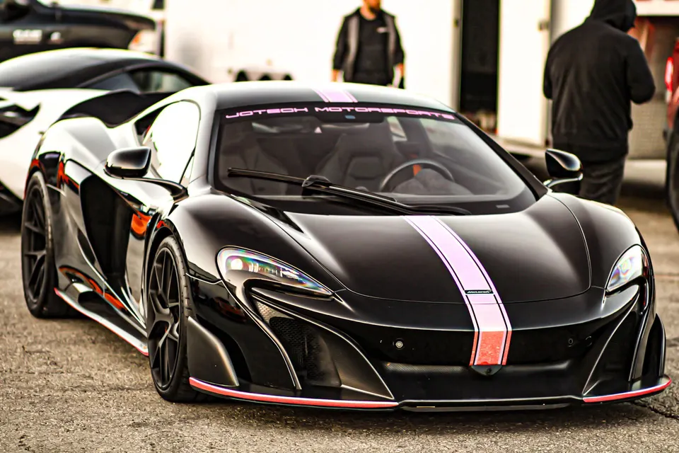 A black McLaren supercar with a pink racing stripe and Jotech Motorsports banner parked outdoors.