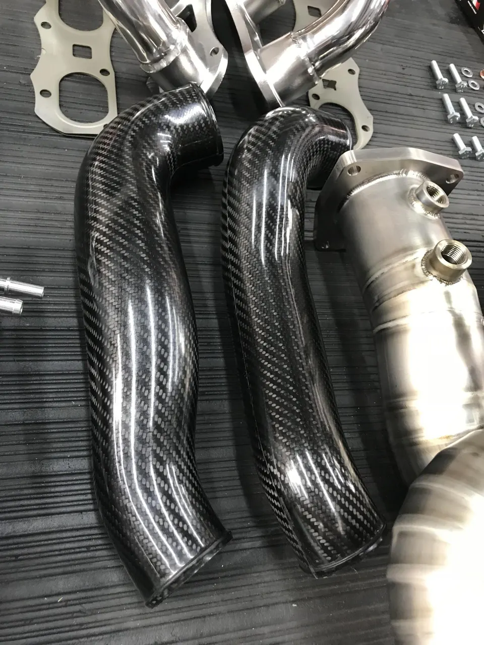 Close-up of carbon fiber boost pipes, polished exhaust headers, and a stainless steel downpipe for a performance build.